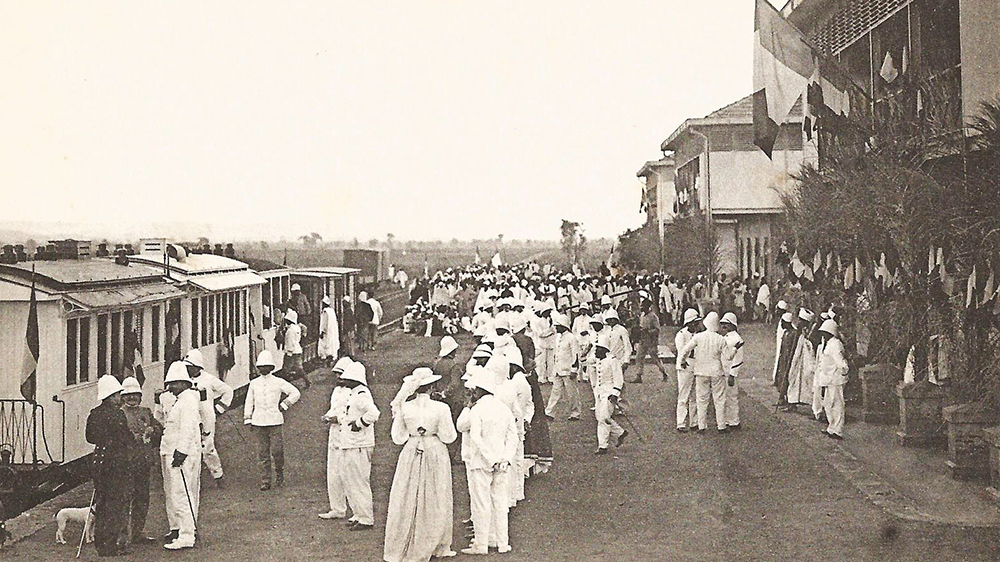 En gruppe mennesker kledd i hvitt står i en gate. Svarthvitt foto. 