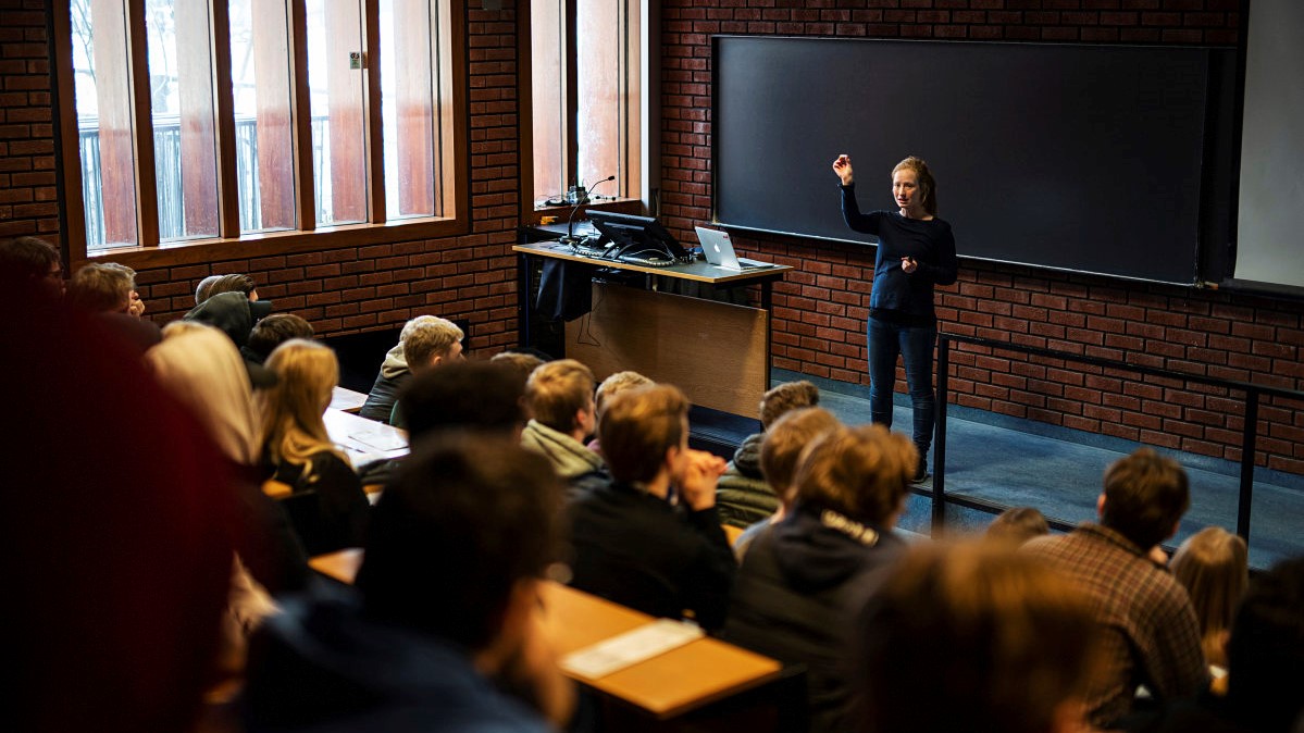 Female lecturer in front of an auditorium full of students. Photo.