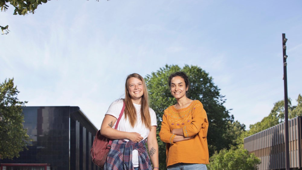 To kvinnelige studenter står på Fredrikkeplassen på Blindern og ser inn i kamera og smiler