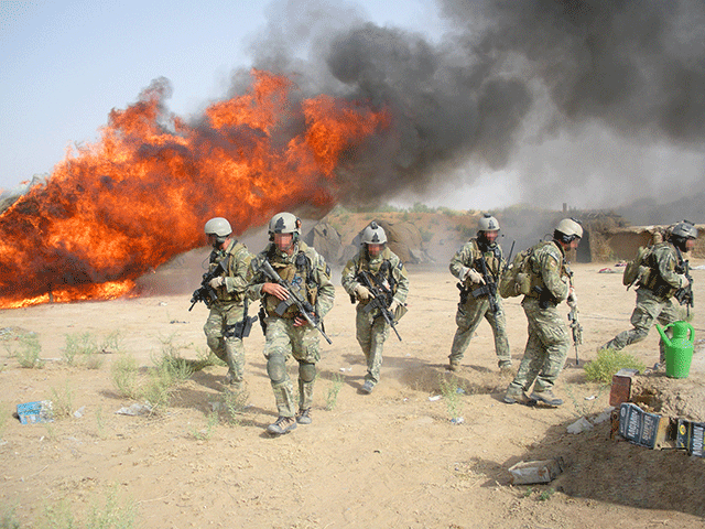 Seks soldater med maskingevær. En kraftig brann i bakgrunnen. Foto. 