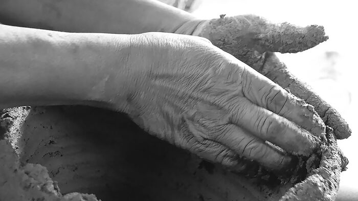 Clos up of two hands chaping a clay bowl. Black and white photo. 
