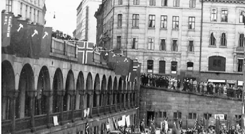 Stort folkehav i et bybilde med norske flagg og flagg med en hammer på. Sort-hvitt foto.