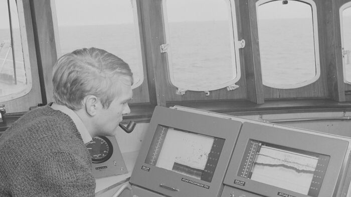 A man on a ship looks at a sonar monitor. Photography. 