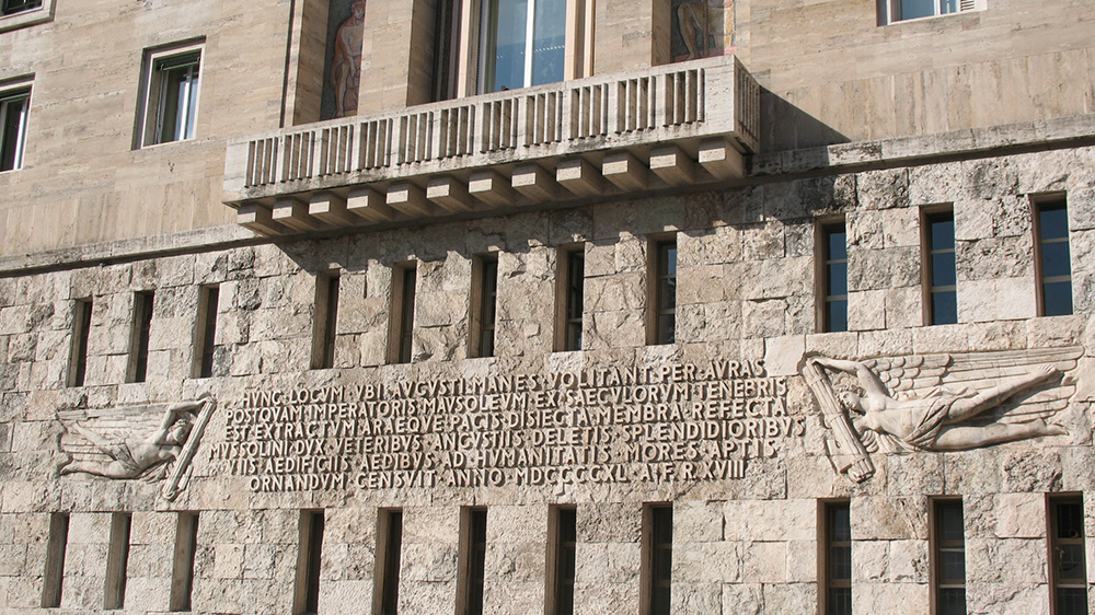 A wall with a balcony and roman letters written on the wall.