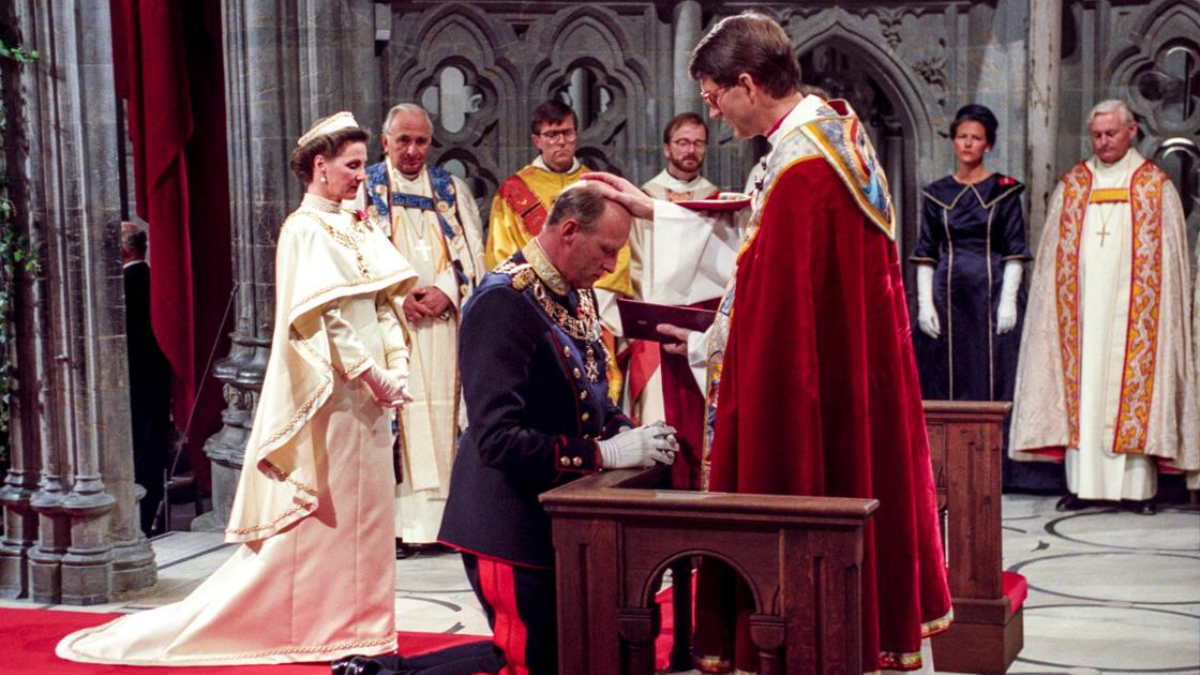 Foto av en kongelig kledd mann som kneler foran en prest, med pent kledde mennesker i bakgrunnen.