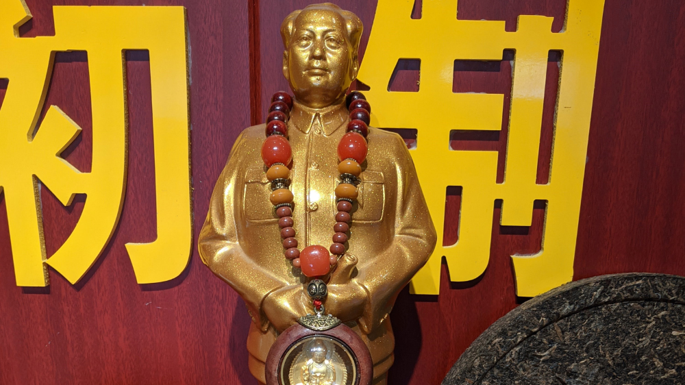 a photo of a statue in gold with a amulet around the neck, with a red background.