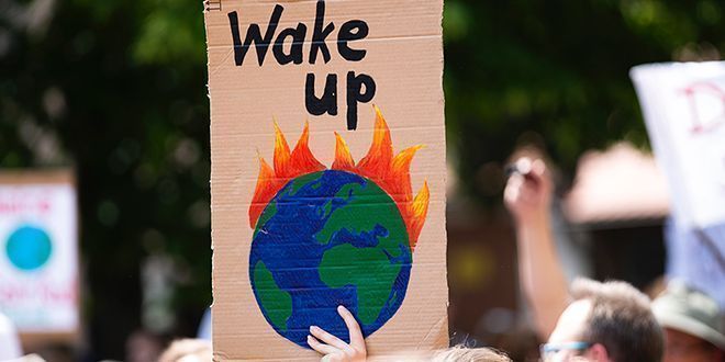Demonstrasjonstog der en hånd holder opp en plakat med bilde av jordkloden som brenner og teksten wake up. Foto.