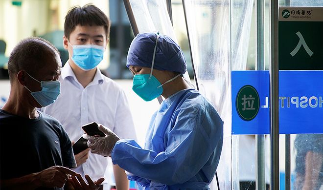 A nurse with blue face mask shows two men wearing face masks something on a smartphone.