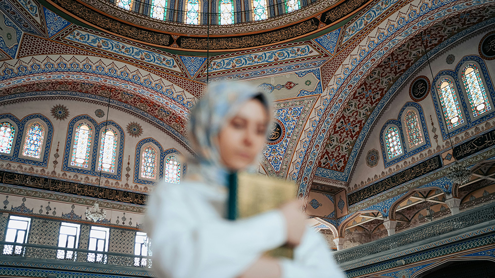 Blurred photo of woman wearing headscarft holding a book.