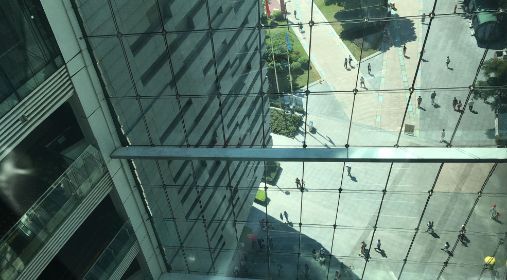 Ser ned på glassvinduer som speiler mange små mennesker på bakkeplan. Biblioteket i Guangzhou. Heading. Foto.