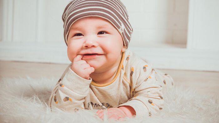 A baby lying on its stomach smiling on a sheepskin on the floor. Photo.