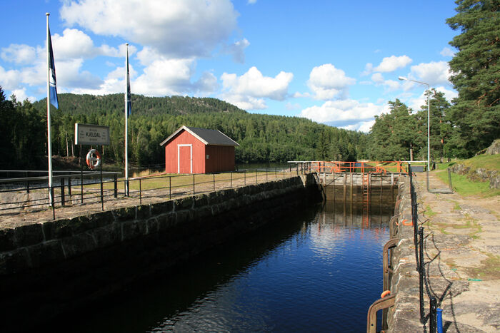 A sluice and a small red house. Green forest in the background.