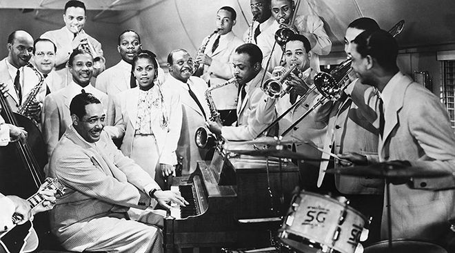 Duke Ellington sitter ved et piano, omgitt av et orkester.