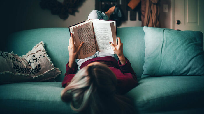 Kvinne leser bok på sofa.