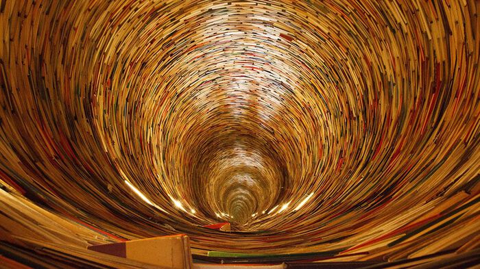 Bøker som ligger stablet og former en lang tunnel. Foto.