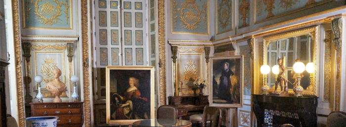 Interiør i et velutsmykket rom med portrettmaleri og gulldetaljer. Parketten er av mørkt og lyst tre lagt i mønster, og det er høyt under taket. Foto.