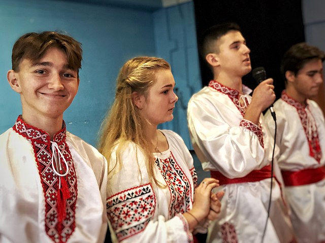 Fire unge ukrainere kledd i tradisjonelle vyshyvankaer synger og smiler. Foto
