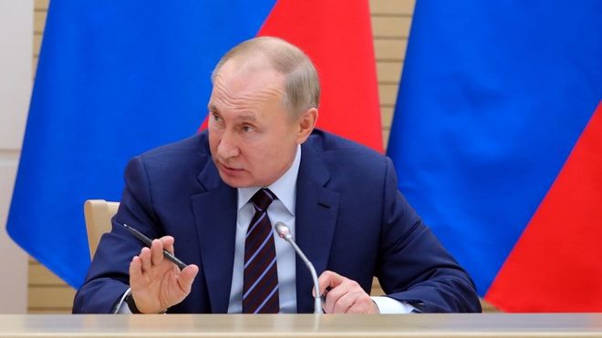 President Vladimir Putin snakker, har russiske flagg bak ham. Foto