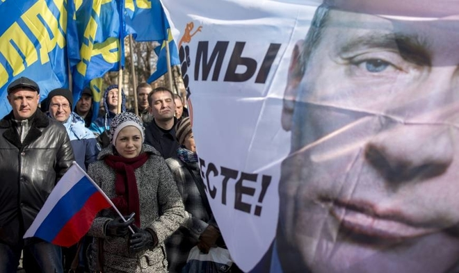 Folk protesterer mot Putin. En dame holder et russisk flagg, og et banner av Putin med slagord mot ham flyr i vinden. Foto