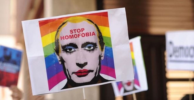 Et bilde av Putins ansikt med sminke, med regnbueflagg i bakgrunnen, med teksten "Stop Homofobia" i pannen hans. Foto