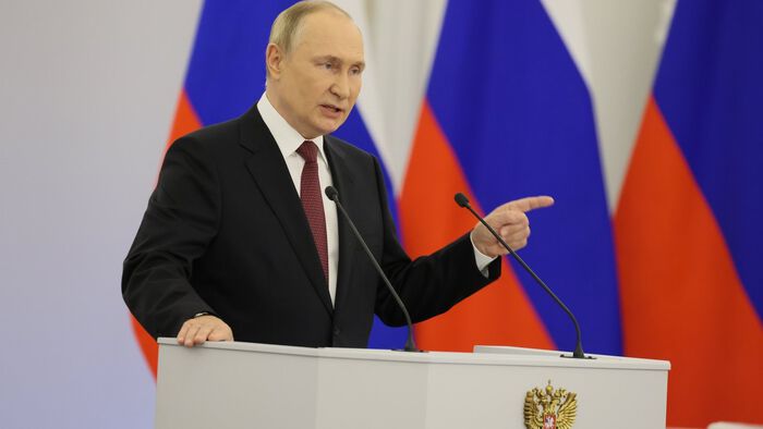 Vladimir Putin står foran et talerbord og med mikrofoner. Bak ham henger tre russiske flagg.