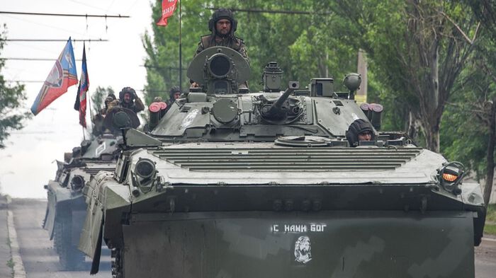 Tre stridsvogner kj?rer i kolonne igjennom en all i Donbass. P? toppen av stridsvognen st?r en soldat. P? stridsvognen st?r det skrevet p? russisk "Gud er med oss". Foto