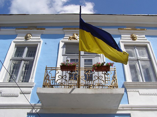 Ukrainsk flagg vaier på en balkong i en pastellblå boligblokk. Foto