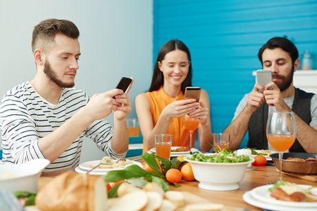 Tre unge mennesker sitter rundt matbordet med hver sin telefon. Foto.