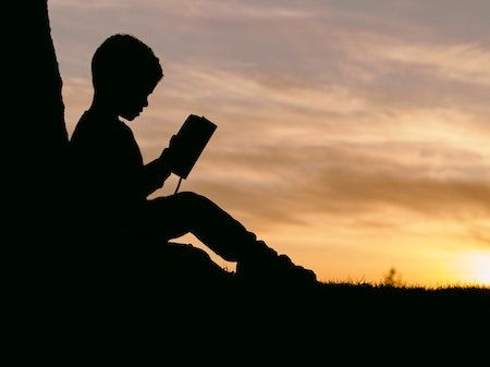 Barn som sitter med bok i solnedgangen