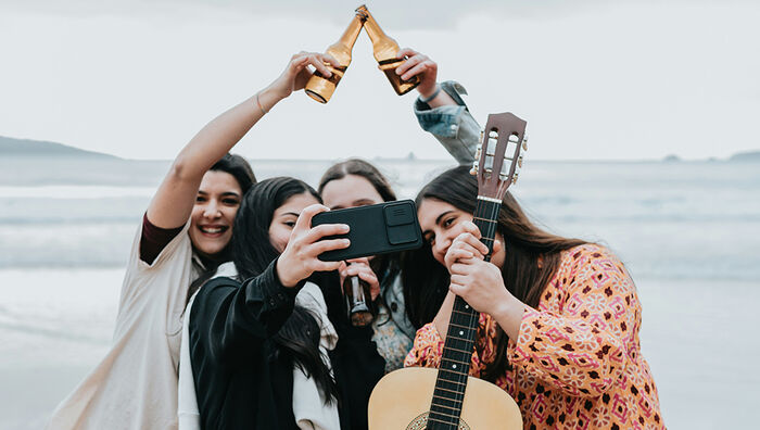 Four women with guitar and bottles taking a selfie. 