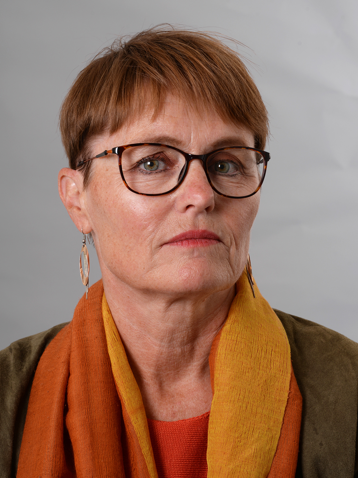 foto av en kvinne med kort brunt hår, briller, og et orange skjerf.