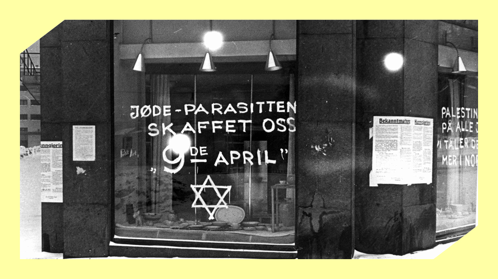Et butikkvindu der det er er skrevet med hvit maling "Jøde-parasitten skafftet oss 9de april" og davidsstjernen. Svart/hvitt foto.