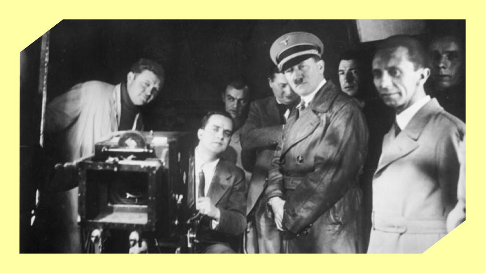 Åtte menn står bak et filmkamera i et filmstudio. Foto.