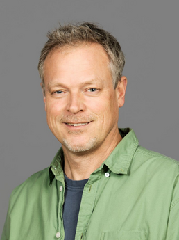 Portrettfotografi av en mann i grønn skjorte som smiler. 