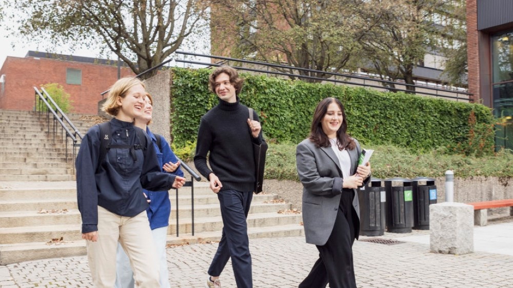 Fire smilende universitetsstudenter med sekk og bøker, går utendørs