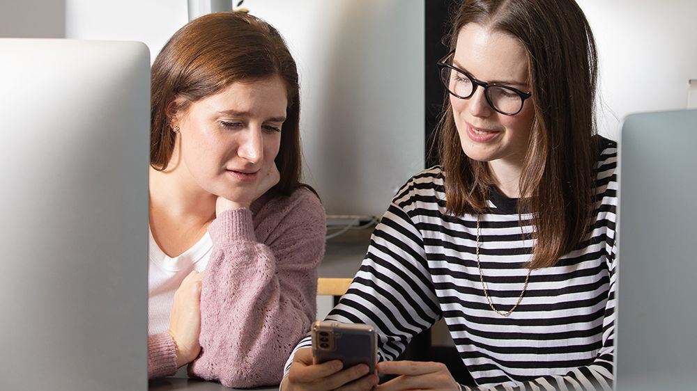 Two young women looks at a smartphone. Photo. 