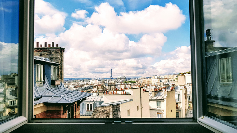 Et åpent vindu med utsikt mot Eiffeltårnet. Foto. 
