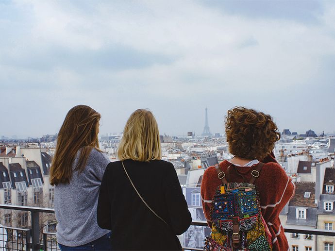 Trois personnes se tiennent debout et regardent la ville de Paris. On peut apercevoir La Tour Eiffel au loin. Photo.