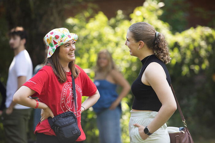 To studenter smiler og prater, hun ene har p? en hatt.