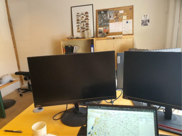 Kontorpult med to dataskjermer, lap-top og kaffekopp