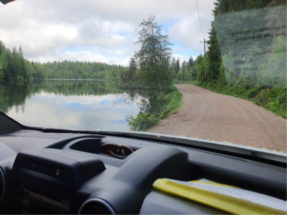 dashboardet til bil på grusdekt vei, vann, skog og skydekt himmel