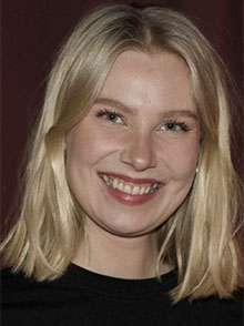 portrettfoto av smilende kvinne, mørk bakgrunn, blondt langt hår, sort genser